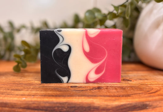 Marbled pink and black soap bar on a wooden surface with greenery in the background