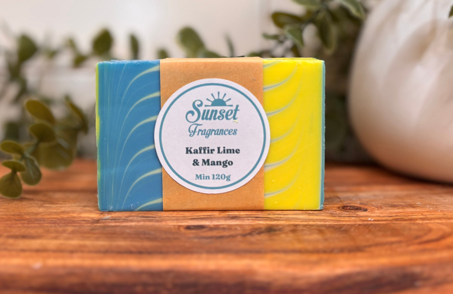 Bar of soap with a colorful packaging on a wooden surface with plants in the background