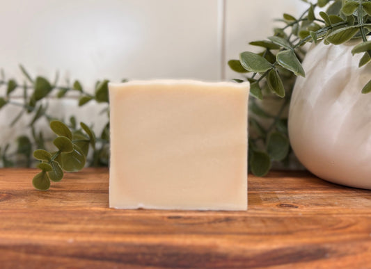 Bar of soap on a wooden surface with plants and a tiled wall in the background