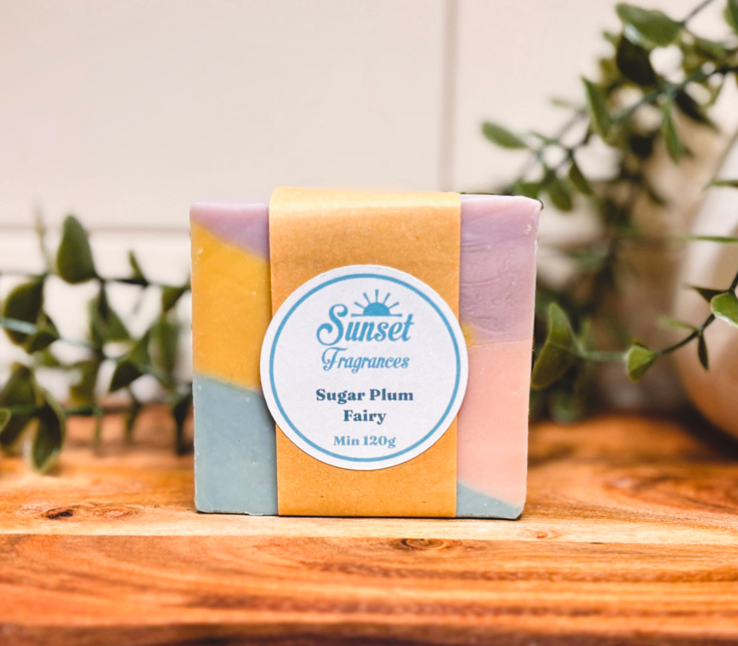 Bar of soap with a colorful packaging on a wooden surface, surrounded by greenery.